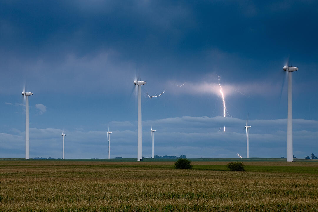 Lightning strikes on the horizon of fields where wind turbines are located.