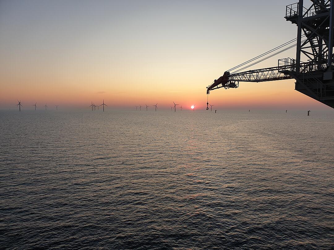 Part of a crane system in front of a wind farm at sea.